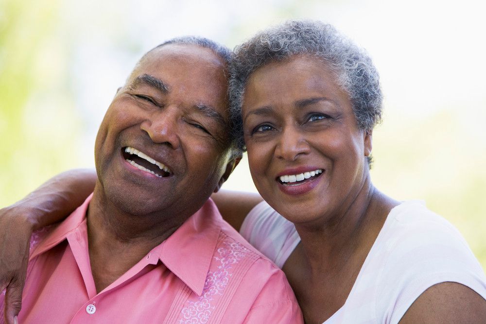 A senior couple sit together, smiling directly at the camera.