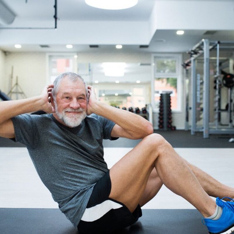 A senior man stays active by doing a floor workout in a bright gym.