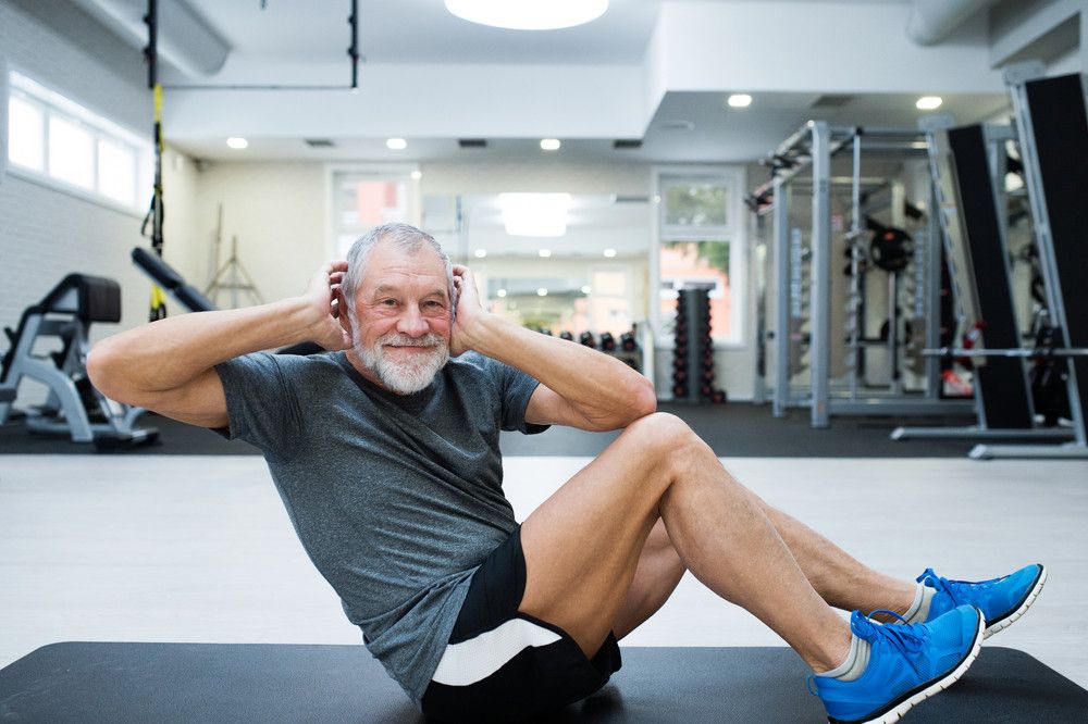 A senior man stays active by doing a floor workout in a bright gym.
